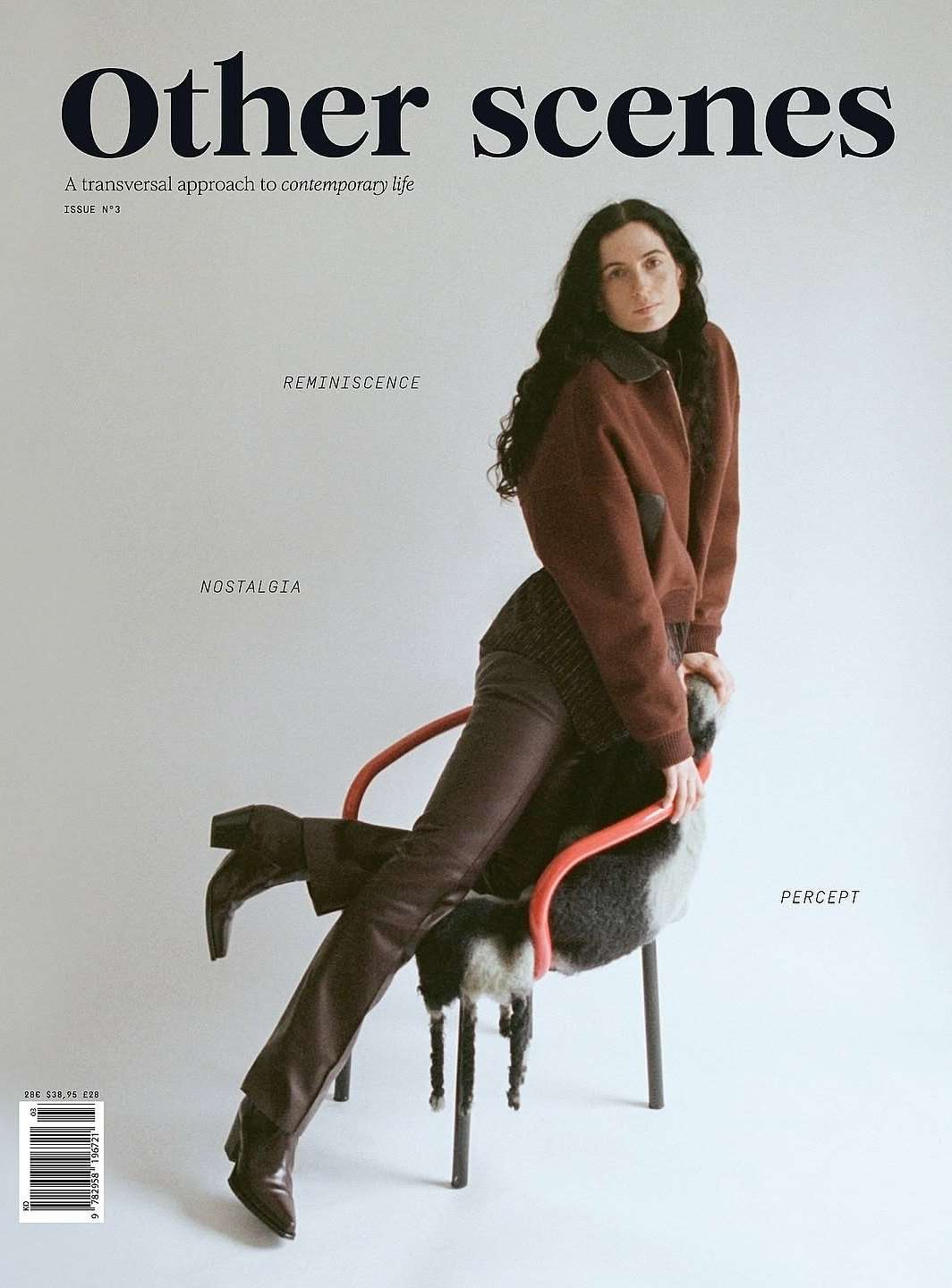 Magazine cover featuring a woman seated on a chair wearing a brown jacket and pants, photographed indoors against a grey backdrop.