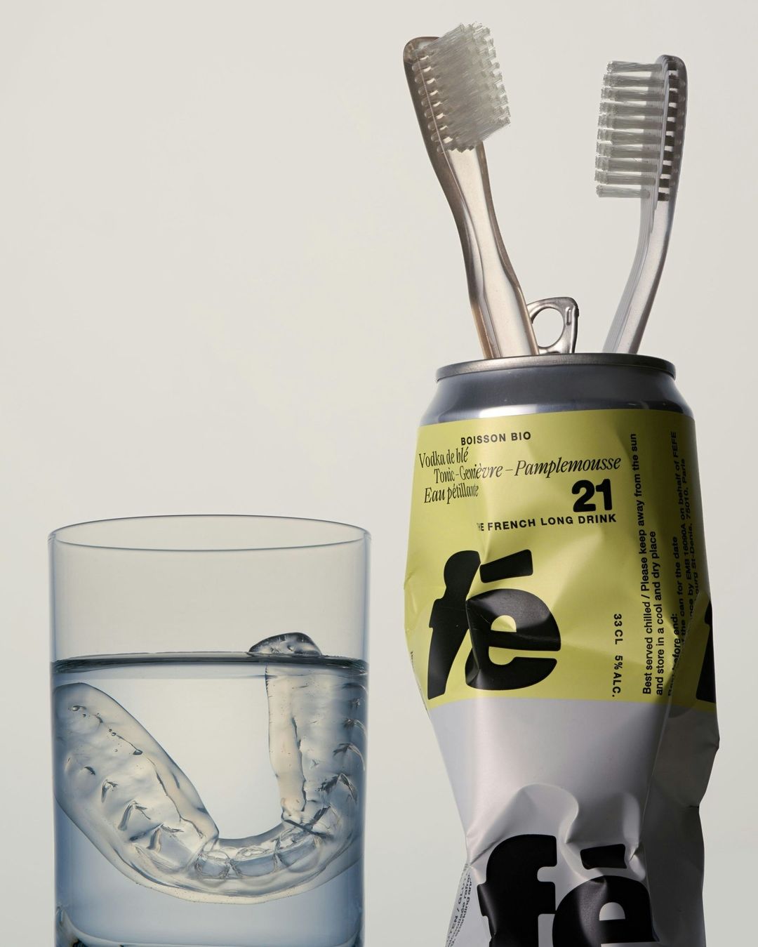 Two toothbrushes in a drink can, clear plastic aligner in a glass of water, on a white background. Hygiene and dental care concept.