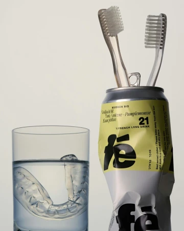 Two toothbrushes in a drink can, clear plastic aligner in a glass of water, on a white background. Hygiene and dental care concept.