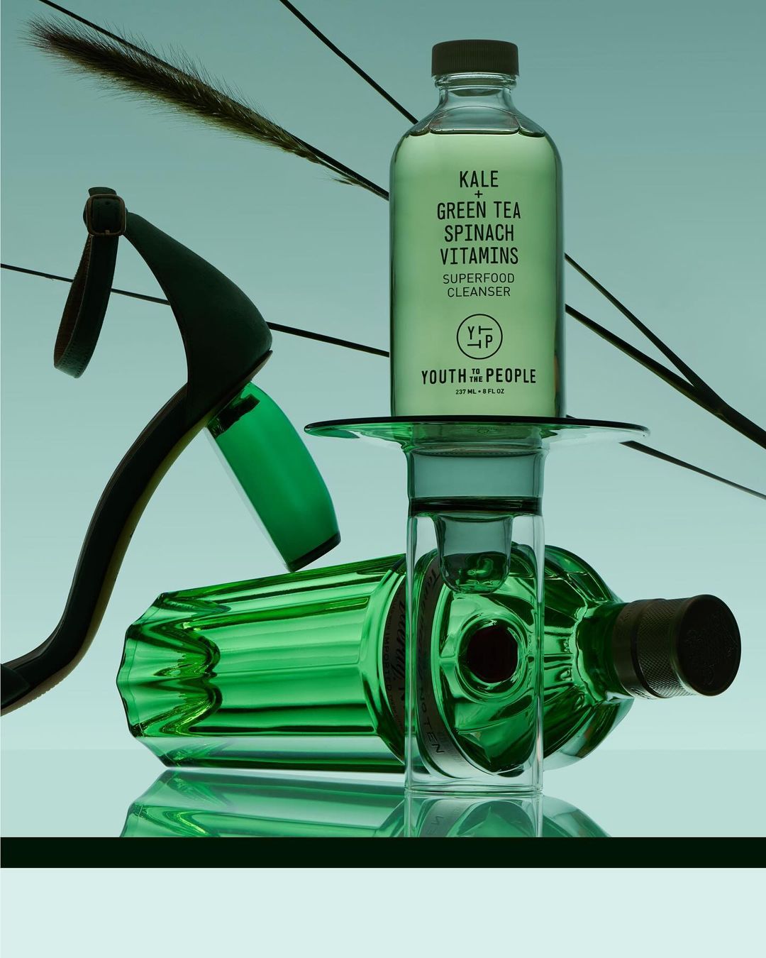 Bottle of Youth to the People Superfood Cleanser displayed with dried floral elements and green glass vials, studio shot against a gradient background.