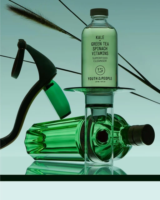 Bottle of Youth to the People Superfood Cleanser displayed with dried floral elements and green glass vials, studio shot against a gradient background.