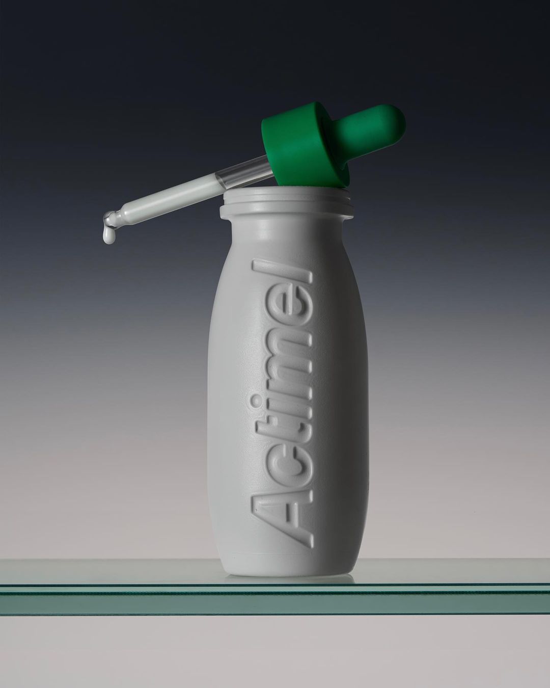 Studio shot of an Actimel bottle with a green dropper, featuring a minimalist composition against a gradient background.