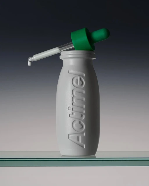 Studio shot of an Actimel bottle with a green dropper, featuring a minimalist composition against a gradient background.
