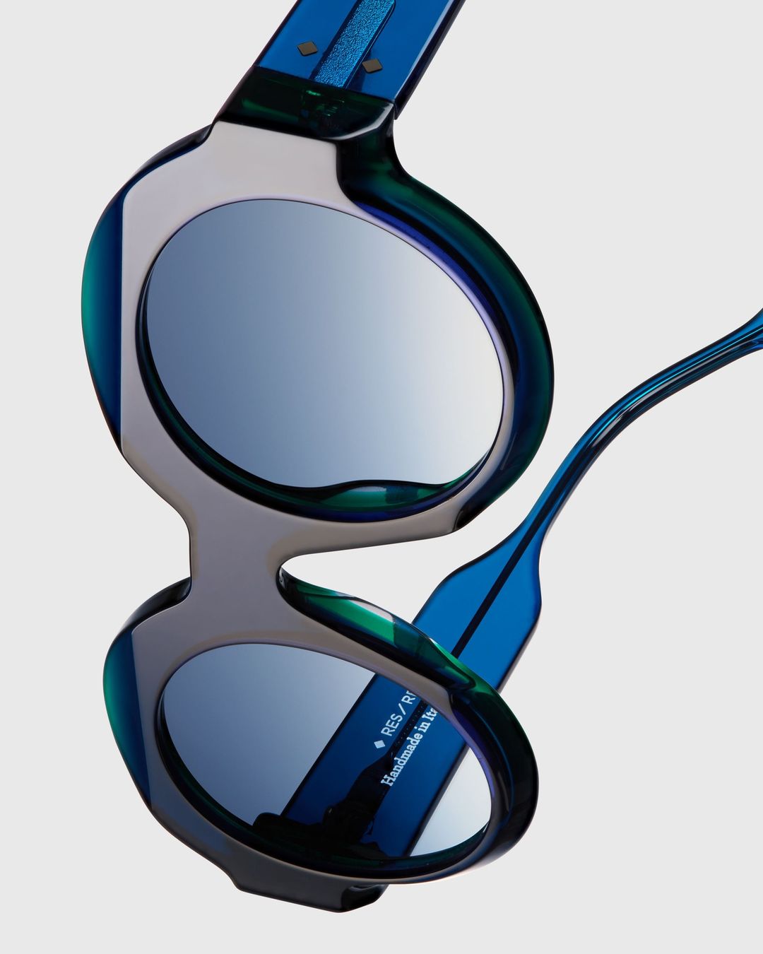 Mirrored lens sunglasses featuring a rounded, teal and blue tinted frame. Close-up studio shot on a white background.