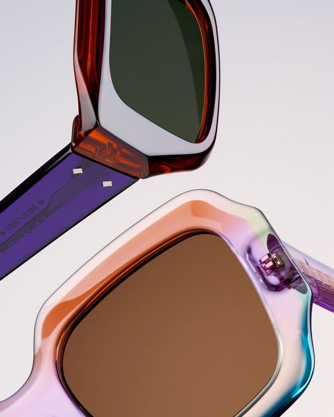 Two pairs of sunglasses are displayed with brown and green lenses. The frames showcase colors of iridescent purple, orange, and white.