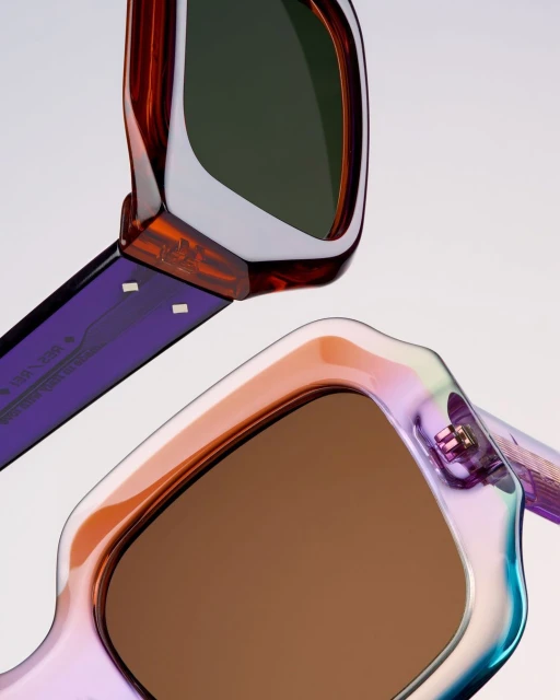 Two pairs of sunglasses are displayed with brown and green lenses. The frames showcase colors of iridescent purple, orange, and white.