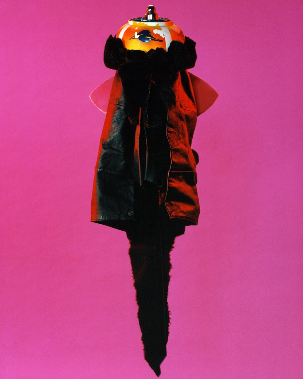 Still life of a black leather coat with fur trim, draped over a mannequin head under lamp, against a vibrant pink background, studio setting.