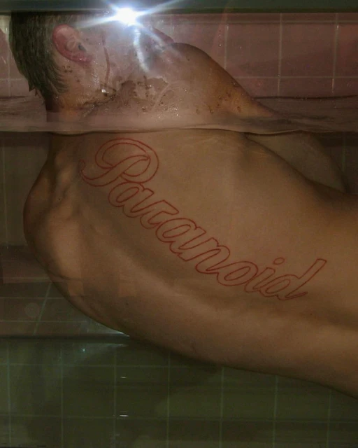 Adult male submerged in water with a "Paranoid" tattoo across his back, creating a striking and evocative visual composition.
