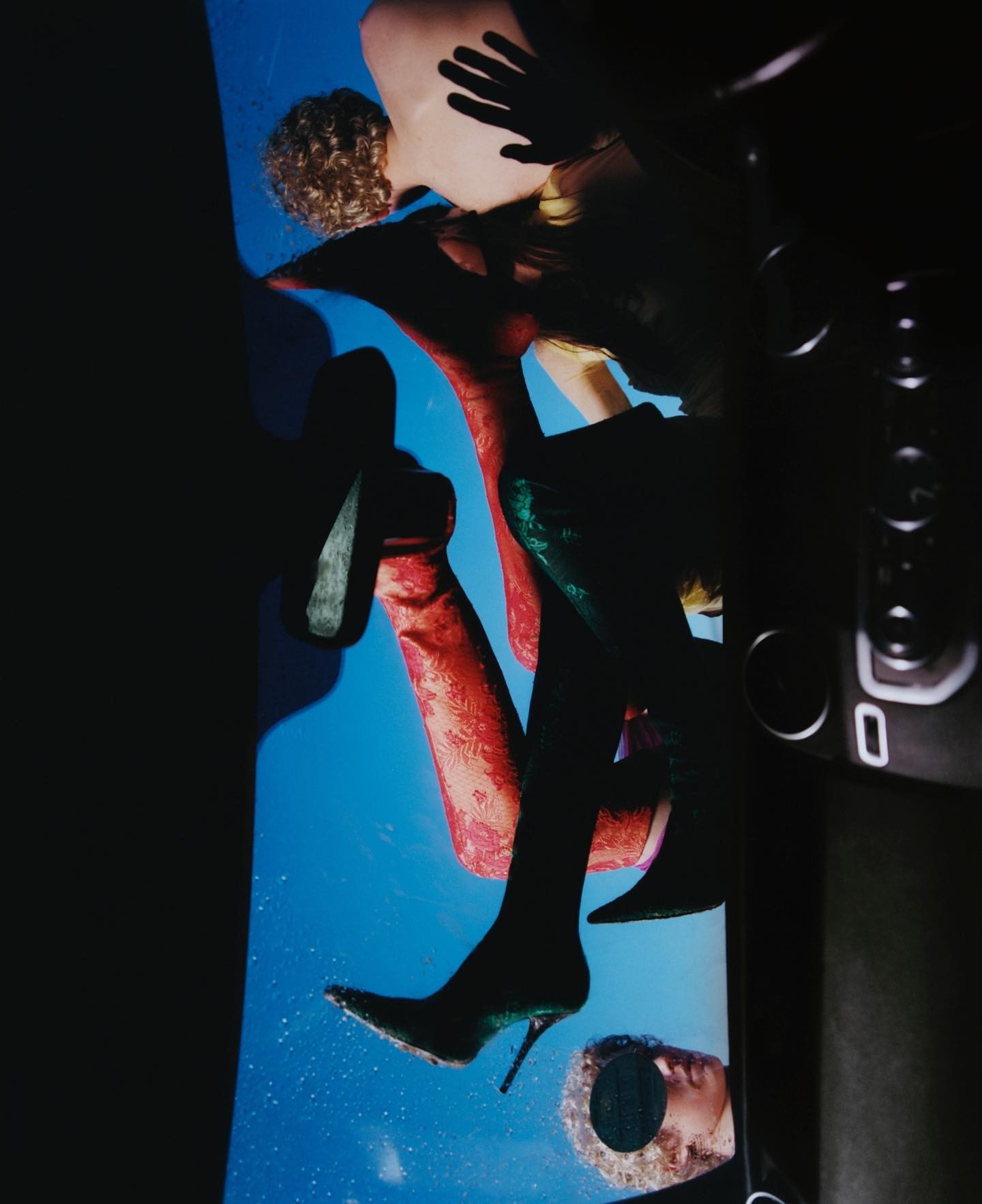 Fashion still life with mannequins, stiletto heels, and studio equipment on a blue background in dark, moody studio lighting.