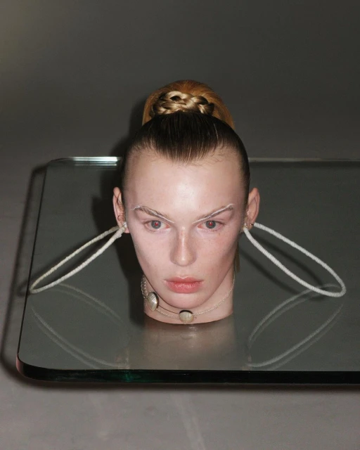 Conceptual fashion shot of a blonde female model with dramatic makeup, a modern necklace, and a futuristic hair style posing indoors.