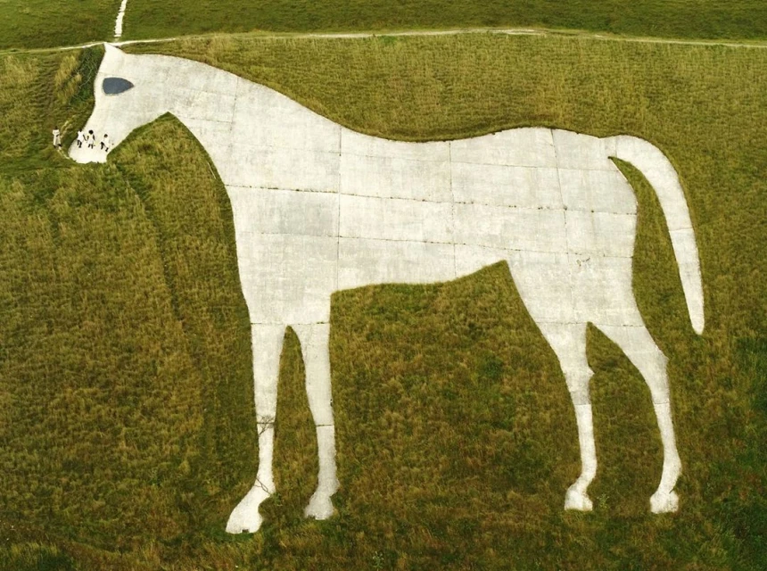 Aerial view of the Uffington White Horse chalk figure in Oxfordshire, England, on a grassy hillside with small group of people nearby.