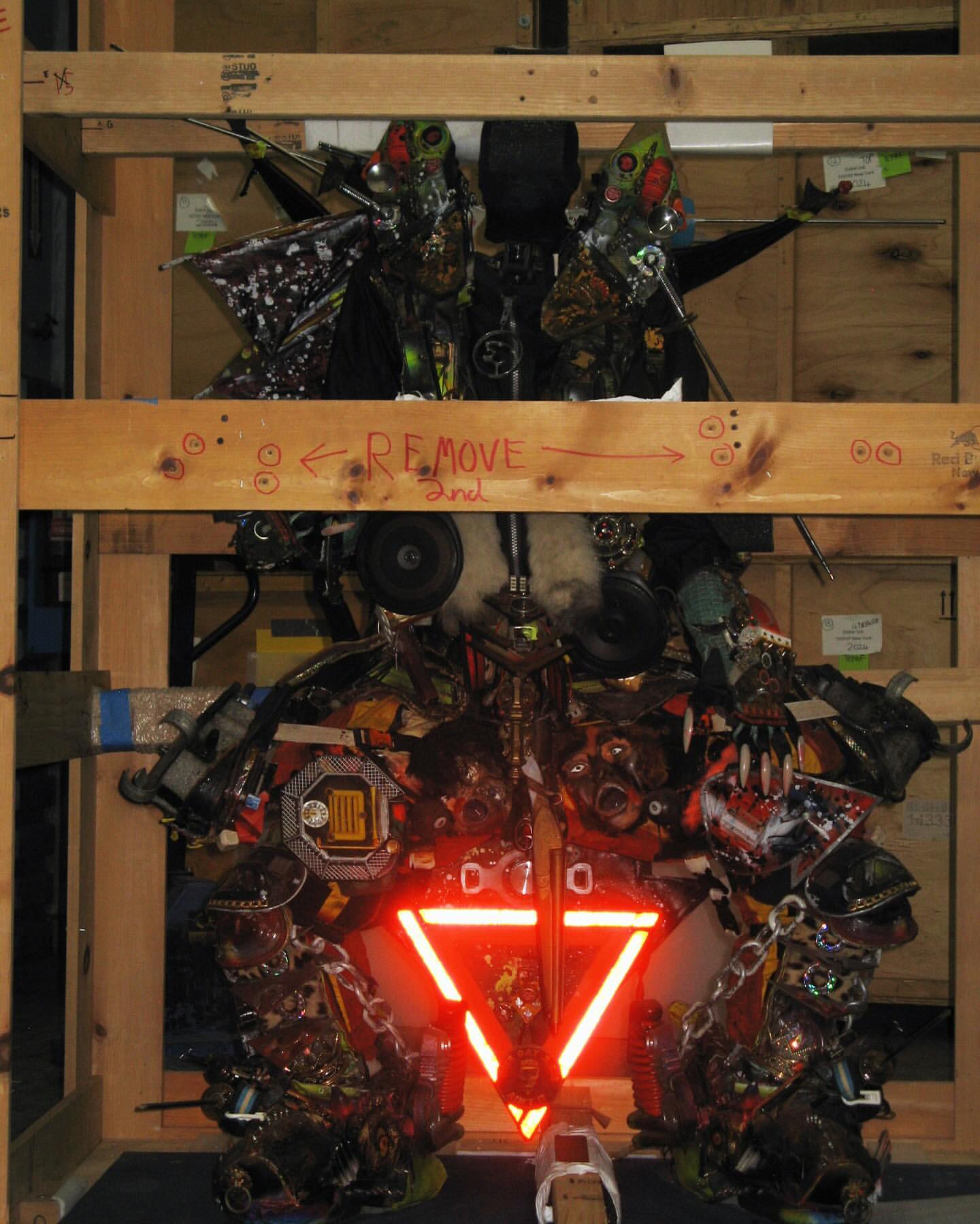Intricate art installation with repurposed materials and a red triangle, set within a wooden frame, showcasing innovative use of recycled elements.