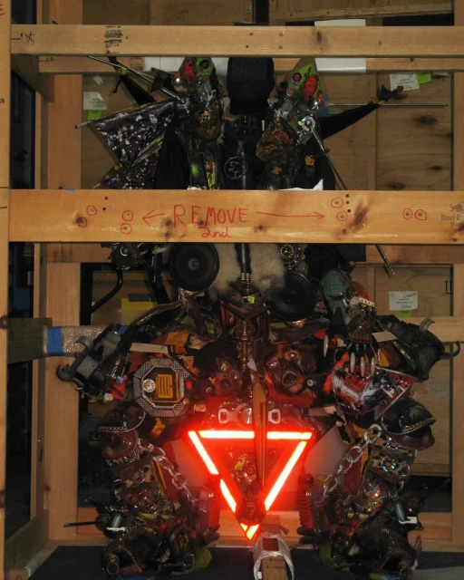 Intricate art installation with repurposed materials and a red triangle, set within a wooden frame, showcasing innovative use of recycled elements.