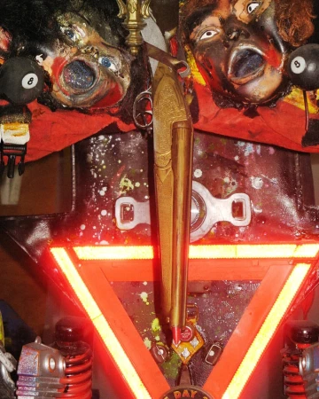 Surreal assemblage art featuring grotesque faces, billiard balls, metallic components, and a glowing red triangular frame, creating a dark and unique scene.
