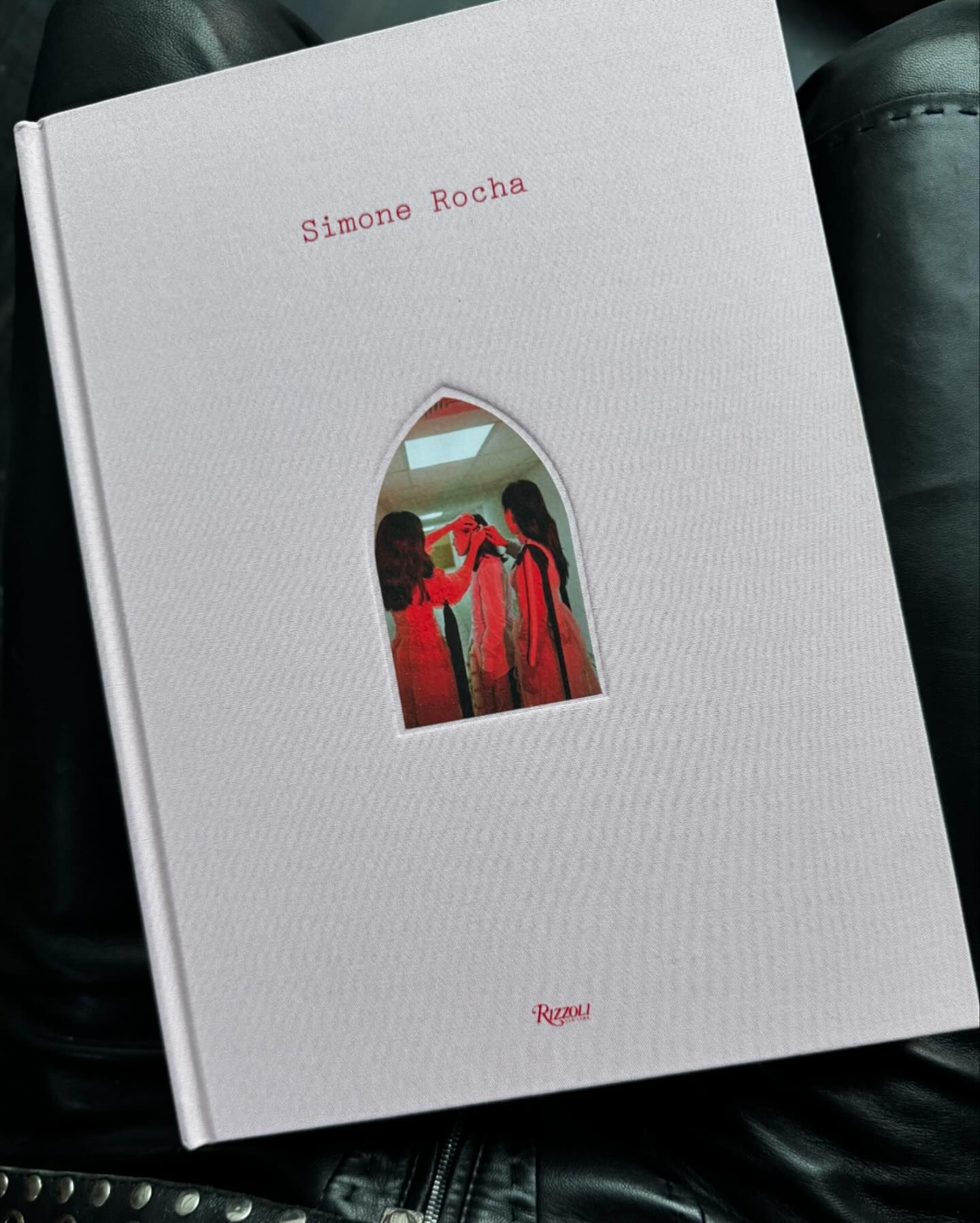Fashion design book by Simone Rocha laying on a black surface featuring two women in red dresses on the book's cover.