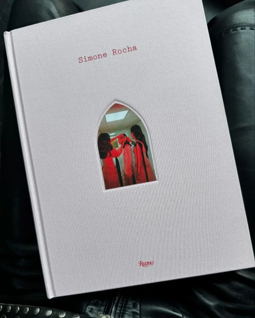 Fashion design book by Simone Rocha laying on a black surface featuring two women in red dresses on the book's cover.