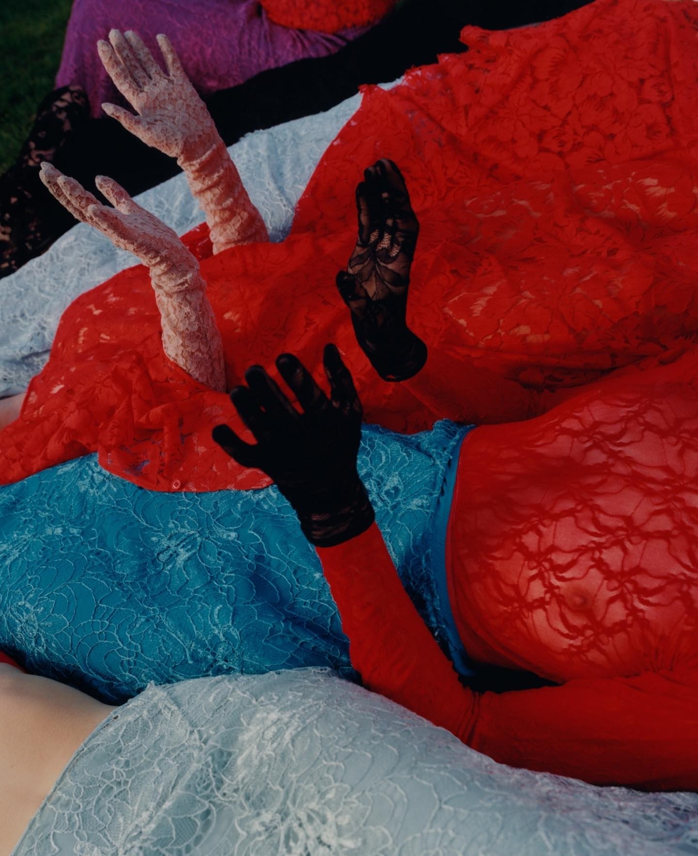 Multiple people wearing colorful lace garments and gloves gesturing with their hands raised against an outdoor ground.