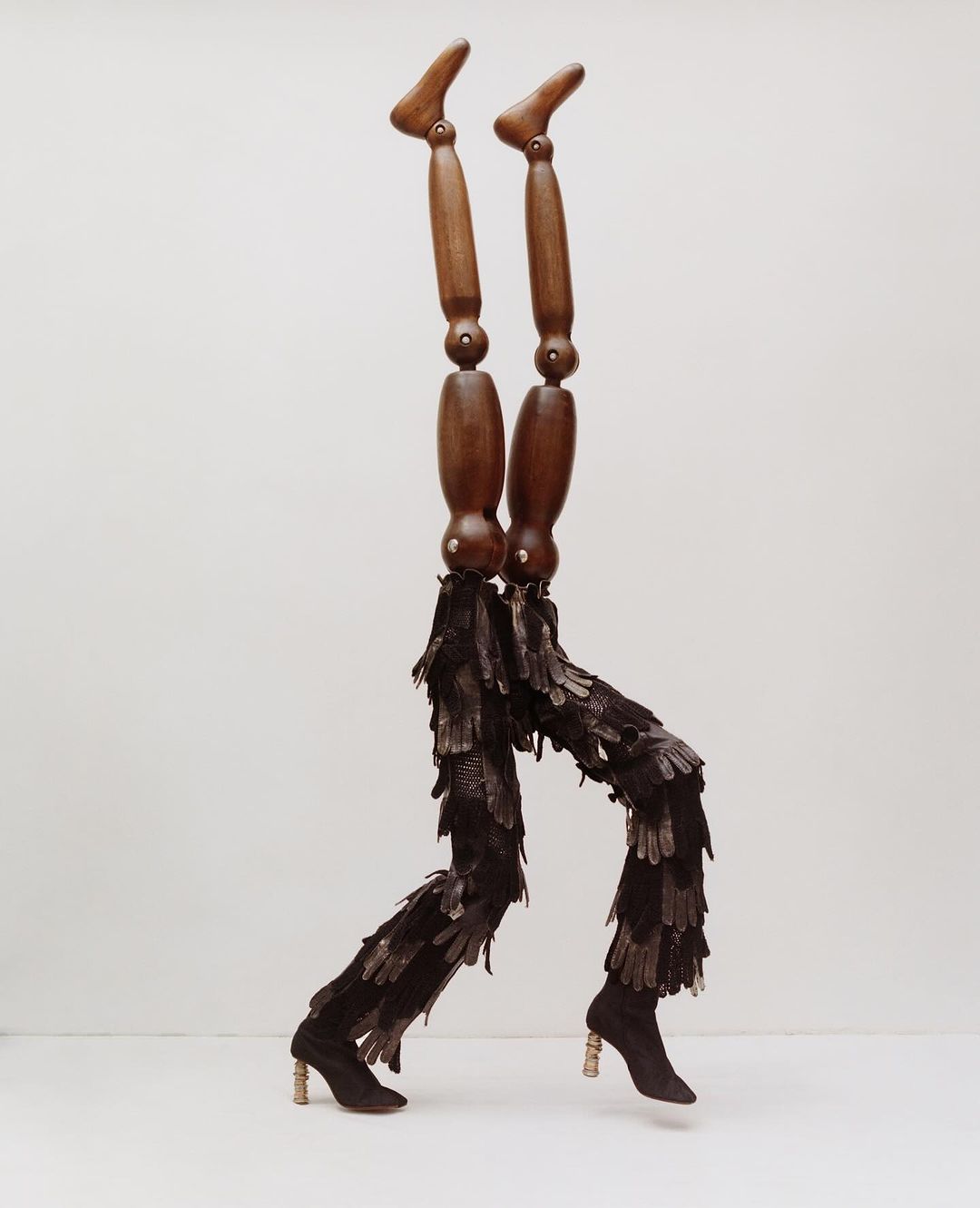 Wooden mannequin legs are adorned with feather-like leggings and heeled booties, all set against a clean, neutral backdrop.