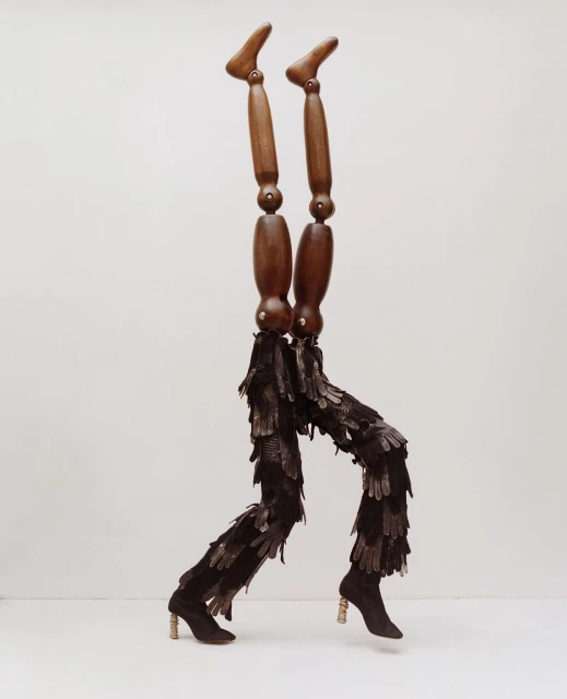 Wooden mannequin legs are adorned with feather-like leggings and heeled booties, all set against a clean, neutral backdrop.