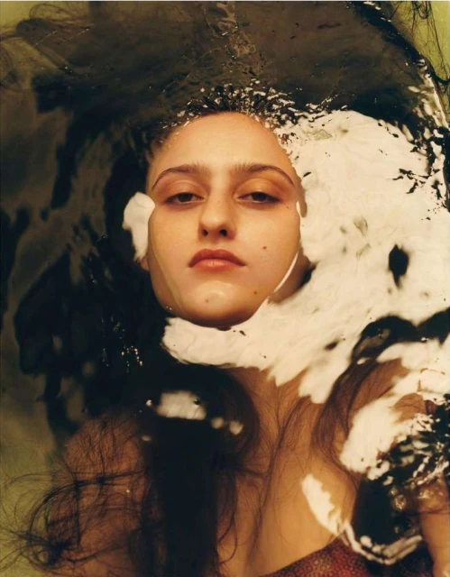 Close-up portrait of a woman with dark hair partially submerged in water, showcasing her face and shoulders in a dark and moody style.