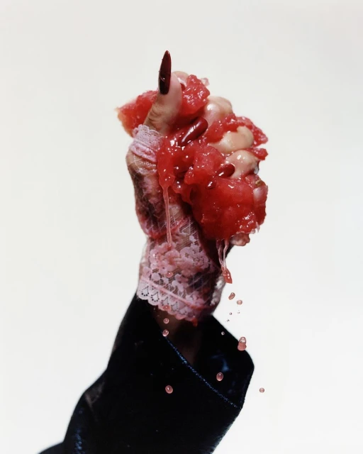 A hand holding a pile of cut-up watermelon, dripping juices against a white background, showcasing a combination of textures and colors.