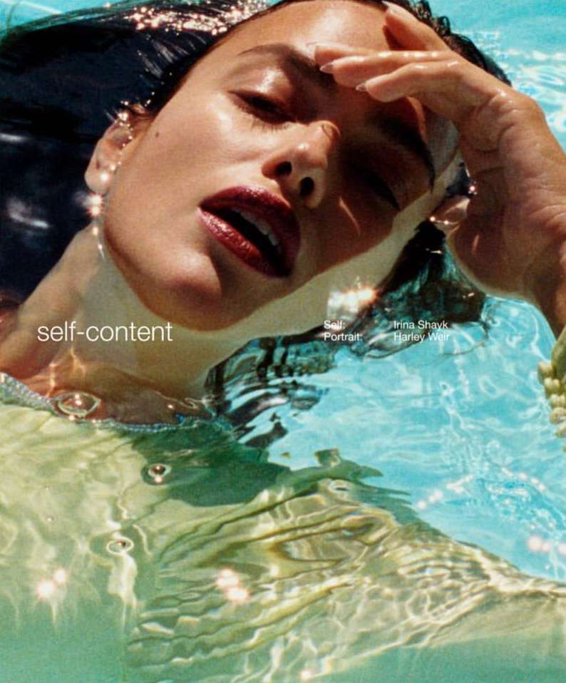 Portrait of adult woman, Irina Shayk, in pool with blue water. Close-up with sunlight and shallow focus on face, red lipstick.