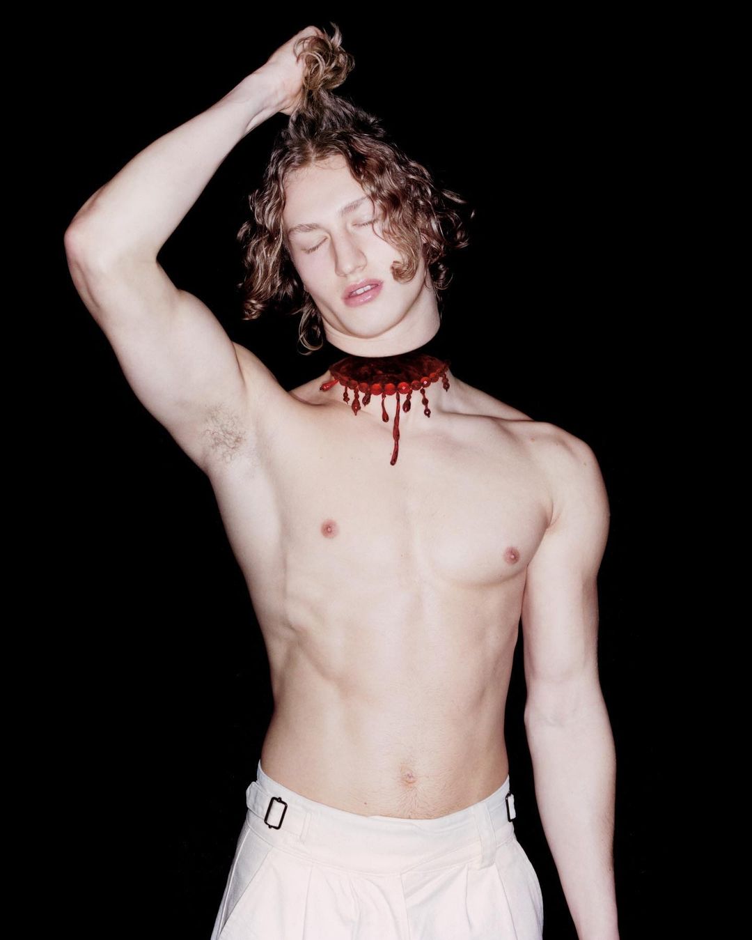 Conceptual portrait of a shirtless male with long wavy hair and a detached head effect against a dark backdrop in a studio setting.