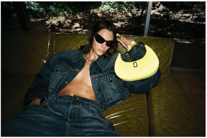A woman in a denim outfit reclines on a sofa with a yellow purse, captured in an indoor setting with natural lighting.