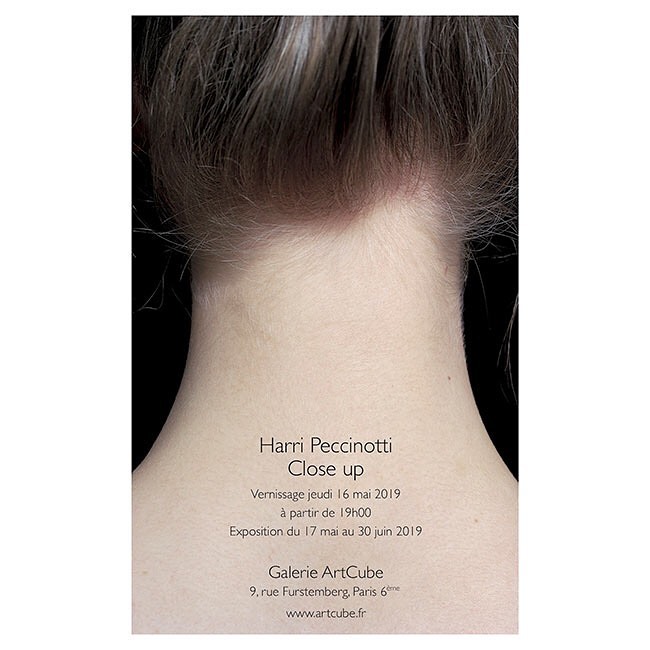 Close-up shot of the back of a woman's neck and head with a promotional poster for an art gallery exhibition in the foreground.