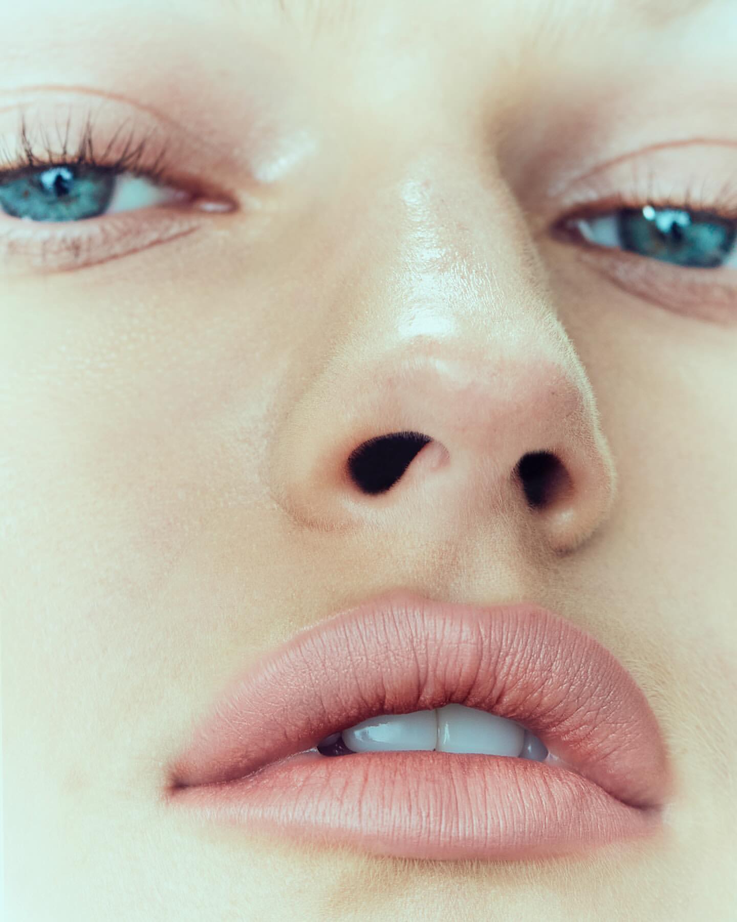 Close-up portrait of a fair-skinned adult female's face featuring clear blue eyes, a defined nose, and full lips with a pink lipstick.