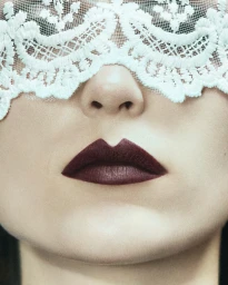 Close-up portrait of a woman wearing a white lace mask over her eyes and dark plum lipstick by Harriet Macsween