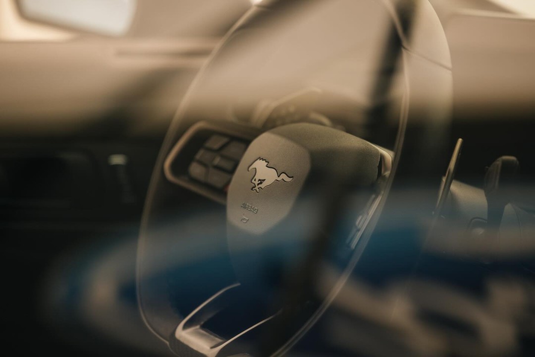 Close-up of a car steering wheel with a horse logo in an interior automotive setting, showcasing the brand's design.