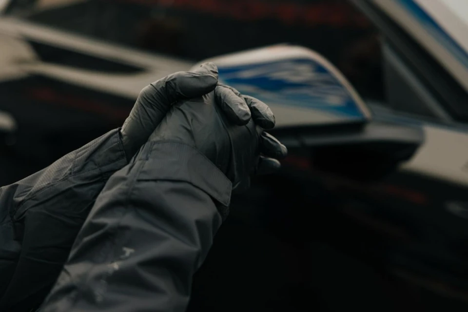 Close-up on black-gloved hands holding a car detail, focusing on the sleek auto body and sky reflection for automotive marketing.