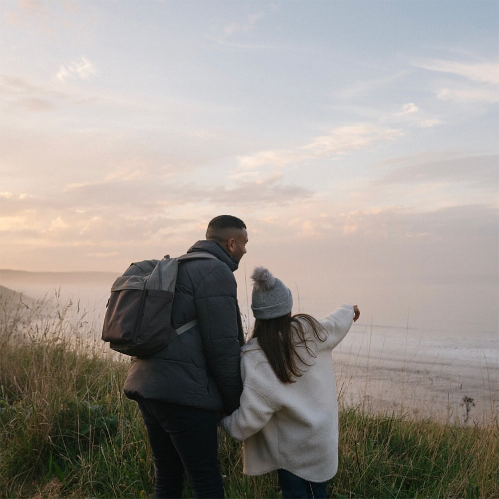 Father and daughter look out at the misty landscape. Man wears a puffy jacket and backpack, while the girl points out at the horizon.