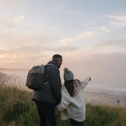Man and woman standing on grassy hill overlooking a misty ocean at sunset, photographed by Harry Hall.