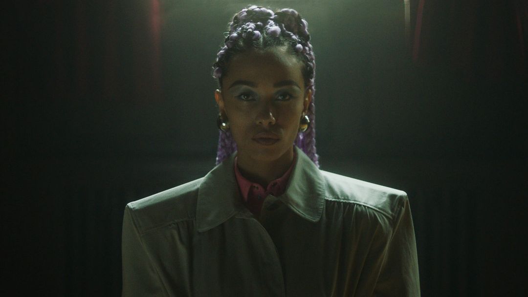 Woman with purple braids in gray coat. Close-up portrait in dark environment with dramatic lighting. Fashion, beauty, and entertainment.