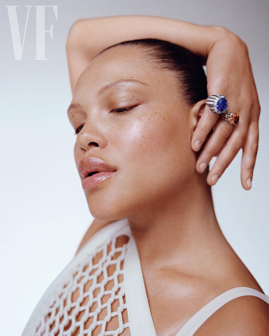 Close-up studio portrait of a Black woman with closed eyes and striking rings, bathed in soft lighting and styled with a white net garment.