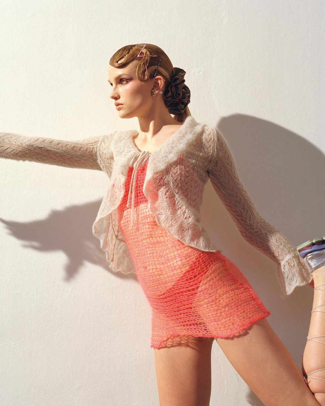 A stylish adult female in a textured peach mini dress with a sheer cardigan poses indoors, accentuated by soft lighting and a neutral background.