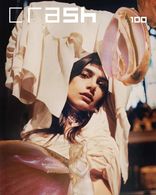 Magazine cover featuring a model with draped fabric and seashell embellishments, showcasing fashion and beauty photography with creative elements.