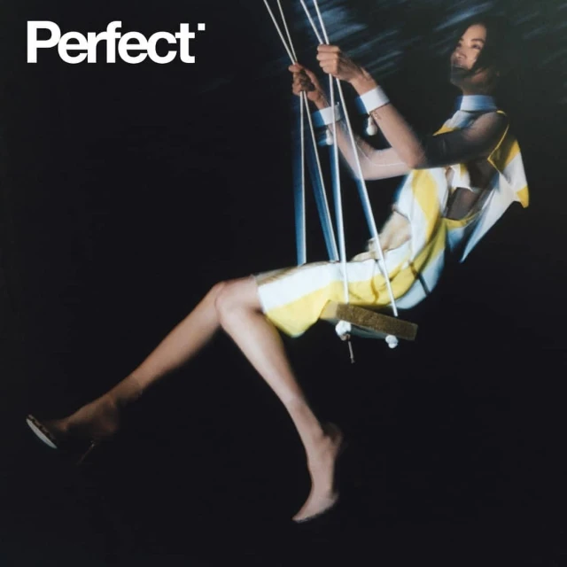 Fashion shot of a slender adult woman sitting on a swing against a black background, wearing a white and yellow striped dress.