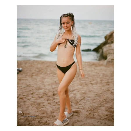Woman with braided hair wearing a black bikini on a sandy beach by the ocean