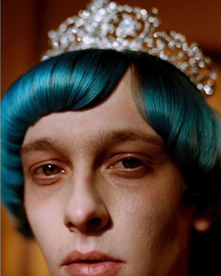 Close-up portrait of an androgynous individual with blue hair and a decorative tiara, showcasing a unique and striking aesthetic.