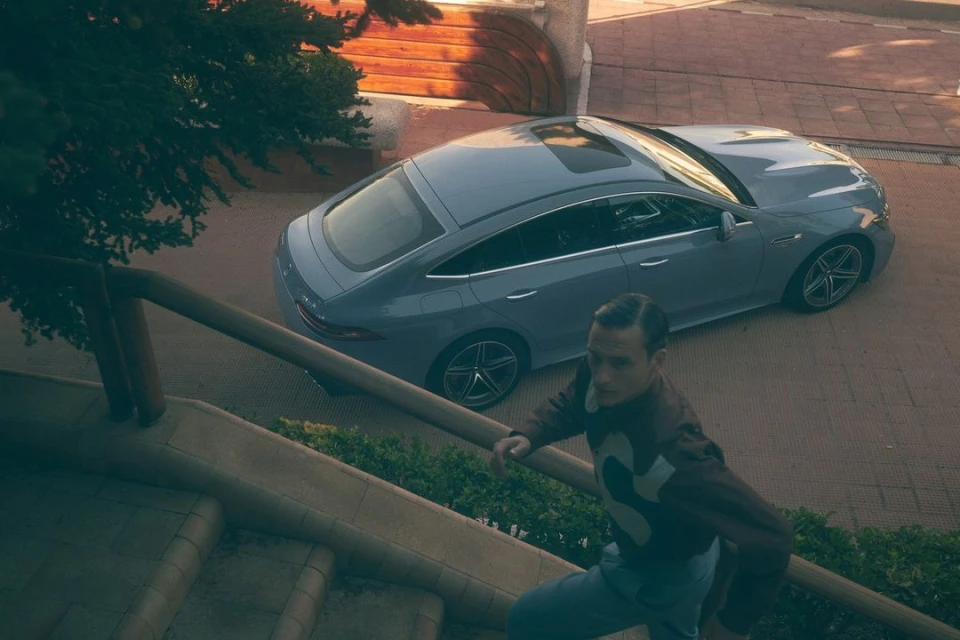 Side view of gray sports car parked on paved surface next to man climbing concrete stairs on sunny day surrounded by greenery.