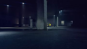 A dimly lit, cavernous parking garage featuring a single yellow car parked under the overhead lights, set against a dark, industrial backdrop.