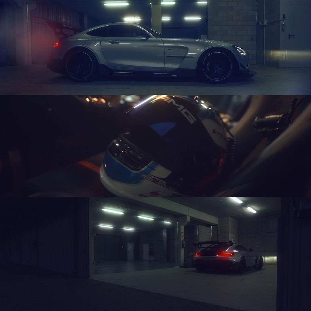 Silver AMG GT parked in a dimly lit parking garage with a racing helmet in the foreground and fluorescent lighting overhead.
