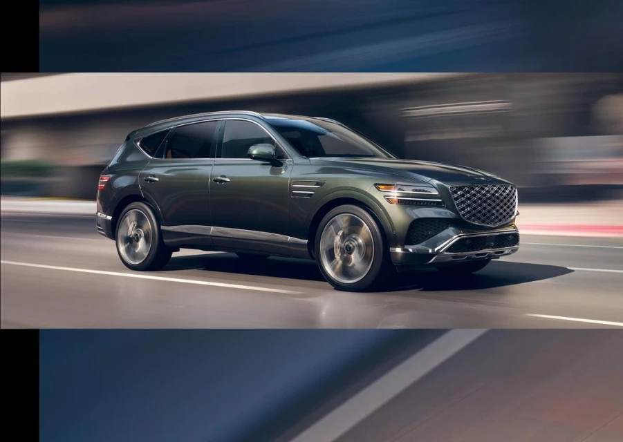 Olive green Genesis SUV speeding on a city road with motion blur. Automotive design featuring a prominent grille and blurred background.