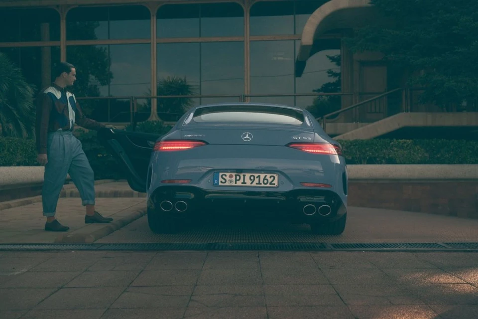 A blue Mercedes-Benz AMG GT 63 stands outdoors with a man opening the driver's side door, under natural lighting.