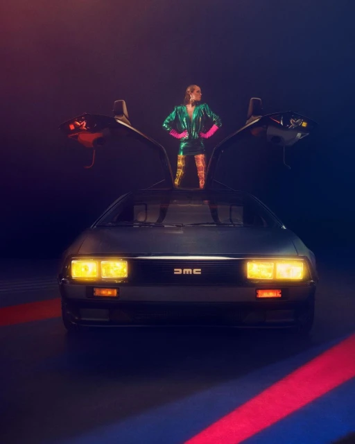 A woman in a green sequin dress and pink gloves standing in front of a DeLorean with open doors, captured in a photo studio.