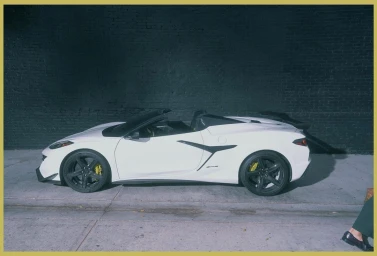 Profile view of a white sports car parked against a dark brick wall in New York photographed by He and Me