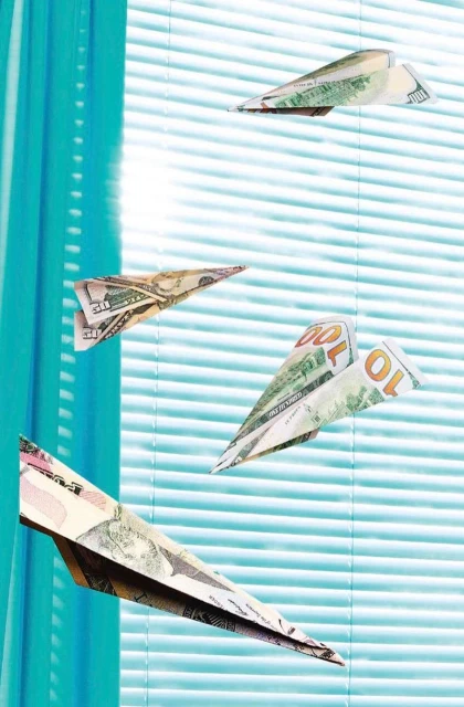 Paper airplanes crafted from US currency float against a backdrop of turquoise window blinds. Playful and financial themed imagery.